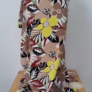 Robe de plage en viscose légère, imprimé fleurs et feuillages beiges, jaune et noirs, drapée sur un mannequin avec coquillages.