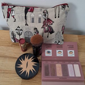 Trousse à maquillage “Shopping” en toile imprimée avec des motifs féminins représentant des silhouettes de femmes élégantes faisant du shopping, sur fond clair, avec une fermeture éclair dorée et intérieur doublé.
