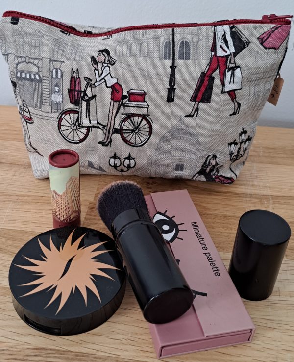 Trousse à maquillage “Shopping” en toile imprimée avec des motifs féminins représentant des silhouettes de femmes élégantes faisant du shopping, sur fond clair, avec une fermeture éclair dorée et intérieur doublé.