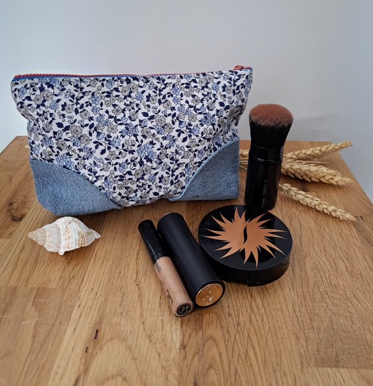 Optez pour cette petite trousse à maquillage pour faire suivre vos essentiels de beauté. Fond blanc et petites fleurs bleues, pieds en Jean, fermeture éclaire rose et doublée en tissu bleu clair uni