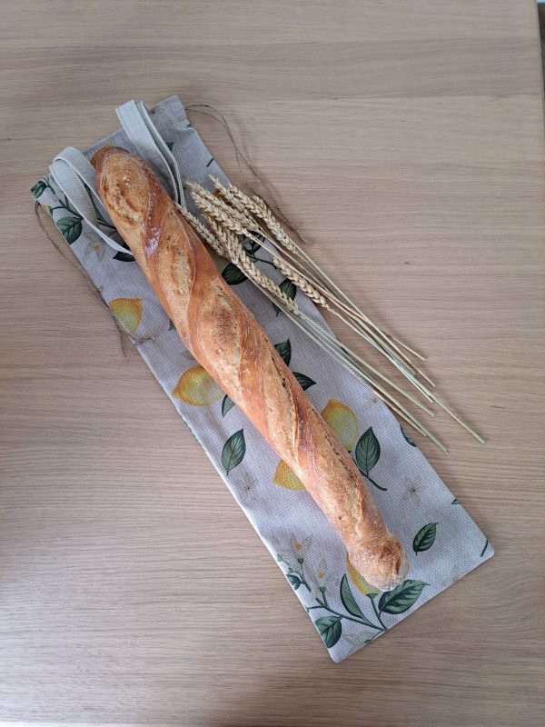 Sac à pain réutilisable Petit Citron posé sur une table, une baguette glissée à l’intérieur, décor citrons — alternative écologique aux sacs et papiers jetables.