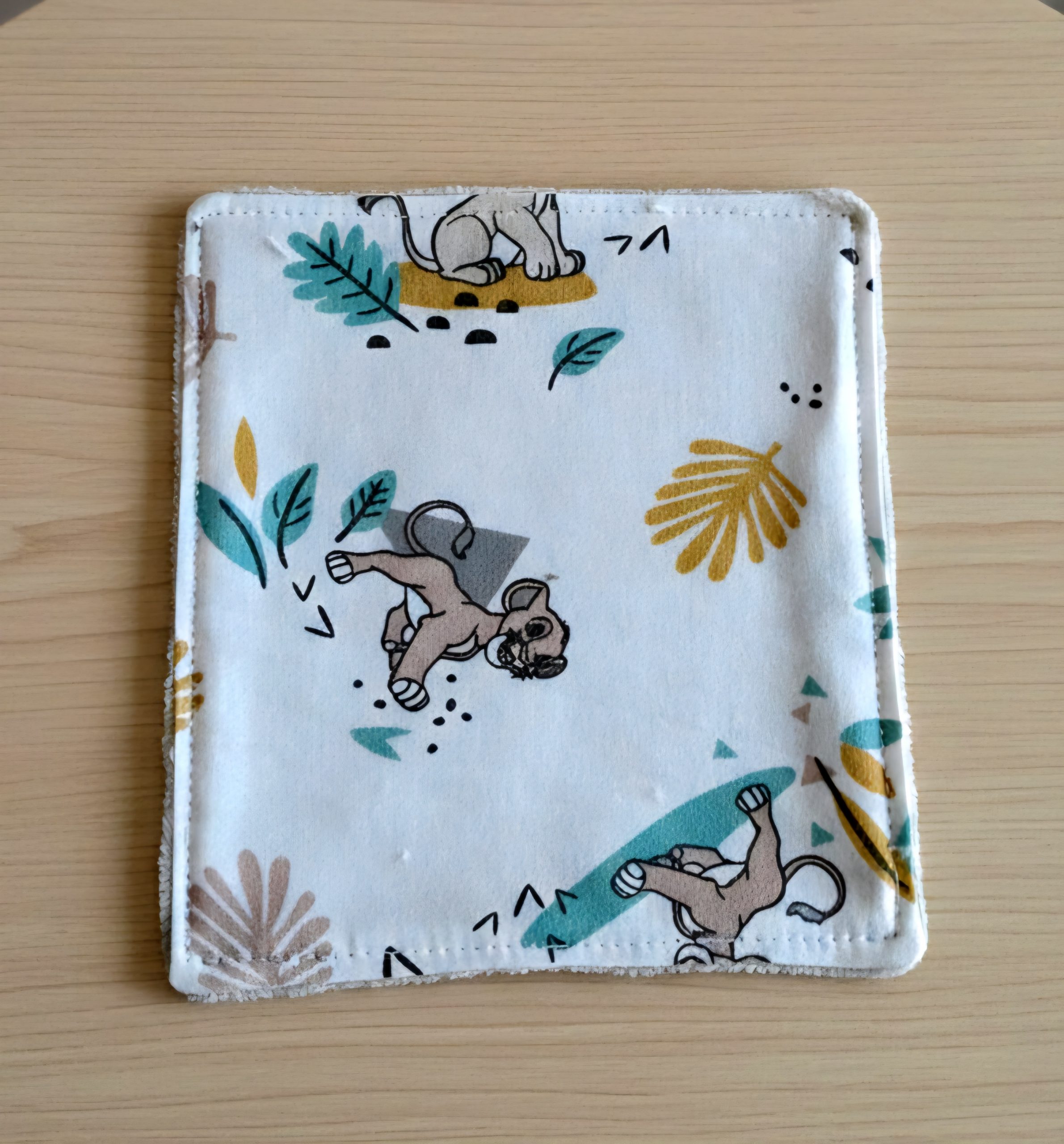 Lot de lingettes lavables artisanales avec motif lionceaux, disposées sur une table en bois pour le change de bébé.