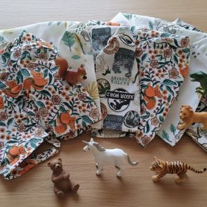 Lot de 6 calots de bloc pédiatriques en tissu avec motifs pour enfants : Cœur de Lionceau, Le Jurassique et Balade en Forêt, étalés sur table en bois.