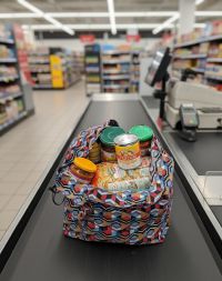 Sac de courses réutilisable style Shupatto rempli de provisions, posé sur une caisse de supermarché.