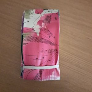 Sac Pli Vite l'Arty en polyester plié à plat sur une table, motifs abstraits artistiques roses et bleus.