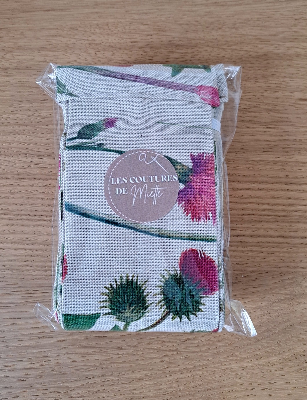 Pochette en tissu au motif floral Bocage, emballée dans un sachet transparent, avec une étiquette ronde “Les Coutures de Miette”, posée sur une surface en bois naturel.