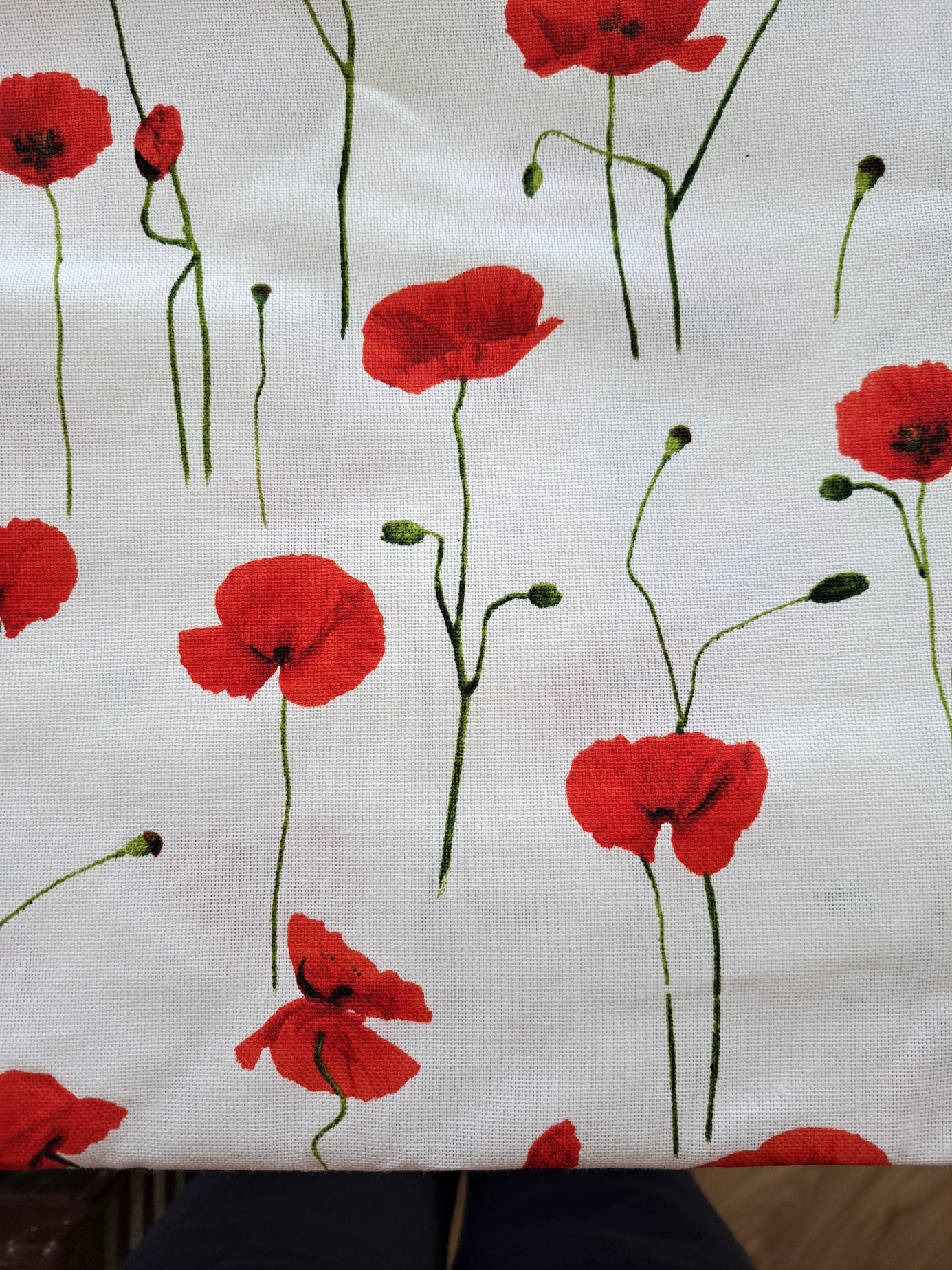 Tissu blanc imprimé de coquelicots rouges et de tiges vertes, avec des fleurs à différents stades d’éclosion, dans un style illustratif lumineux et naturel.