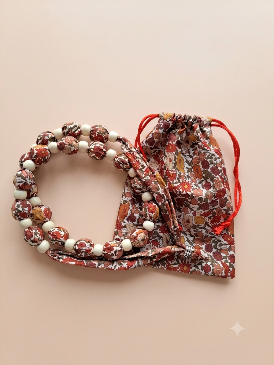 Collier Éclisse en tissu Liberty avec sa pochette assortie, perles textiles florales et finitions artisanales. alt‑text Éclisse